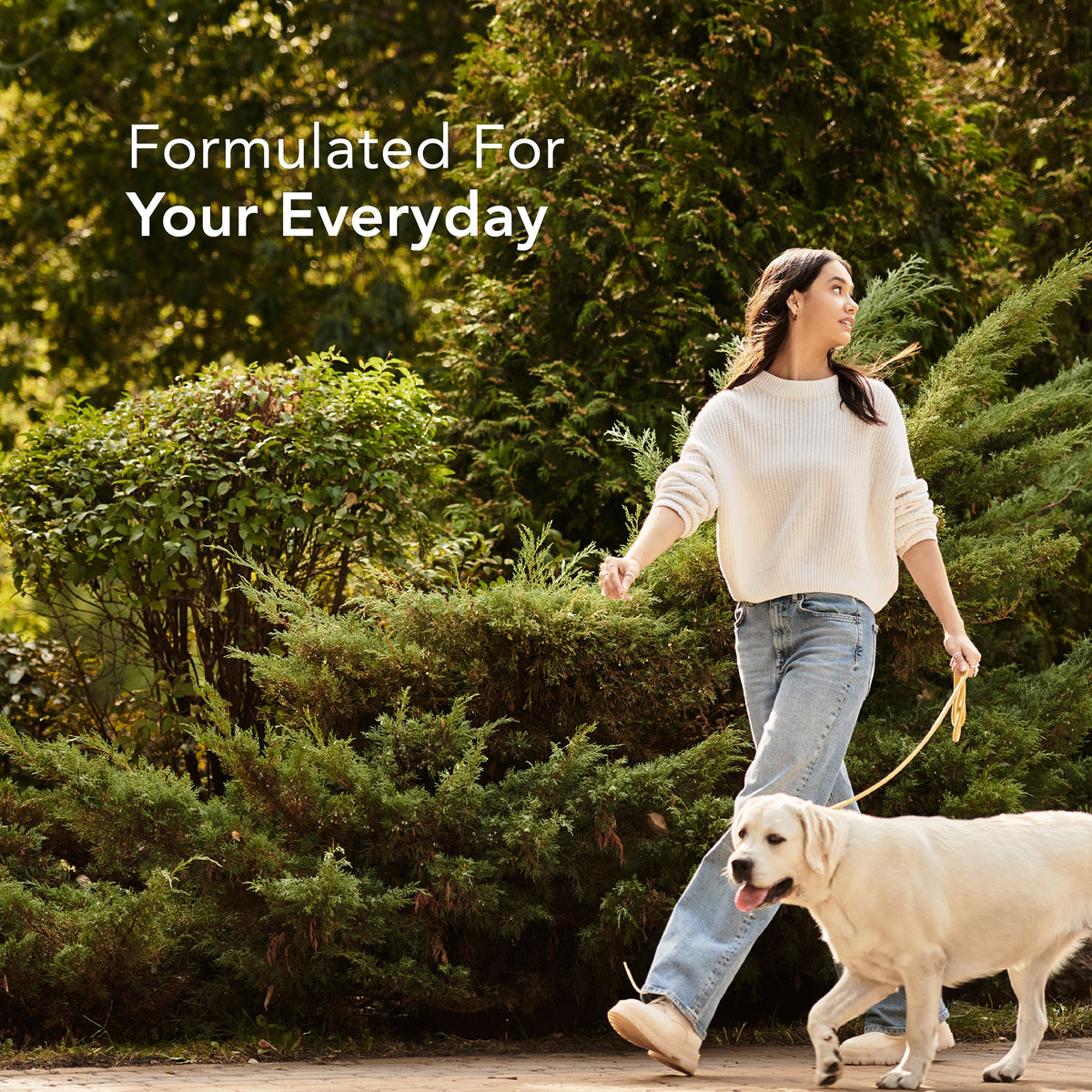 A young woman walking a golden retriever on a leash outdoors with the text 'Formulated For Your Everyday'.