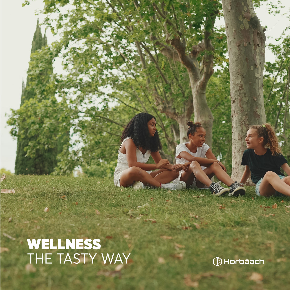 Three young girls sit on the grass and chat in a park.