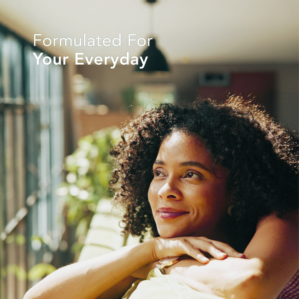 Young woman smiles while holding a Fenugreek supplement, gazing thoughtfully out a window.