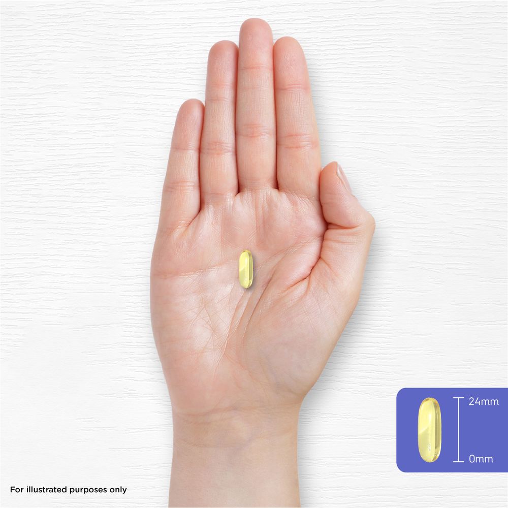 A yellow softgel, 24mm in length, rests on a person's palm, illustrating size and scale.
