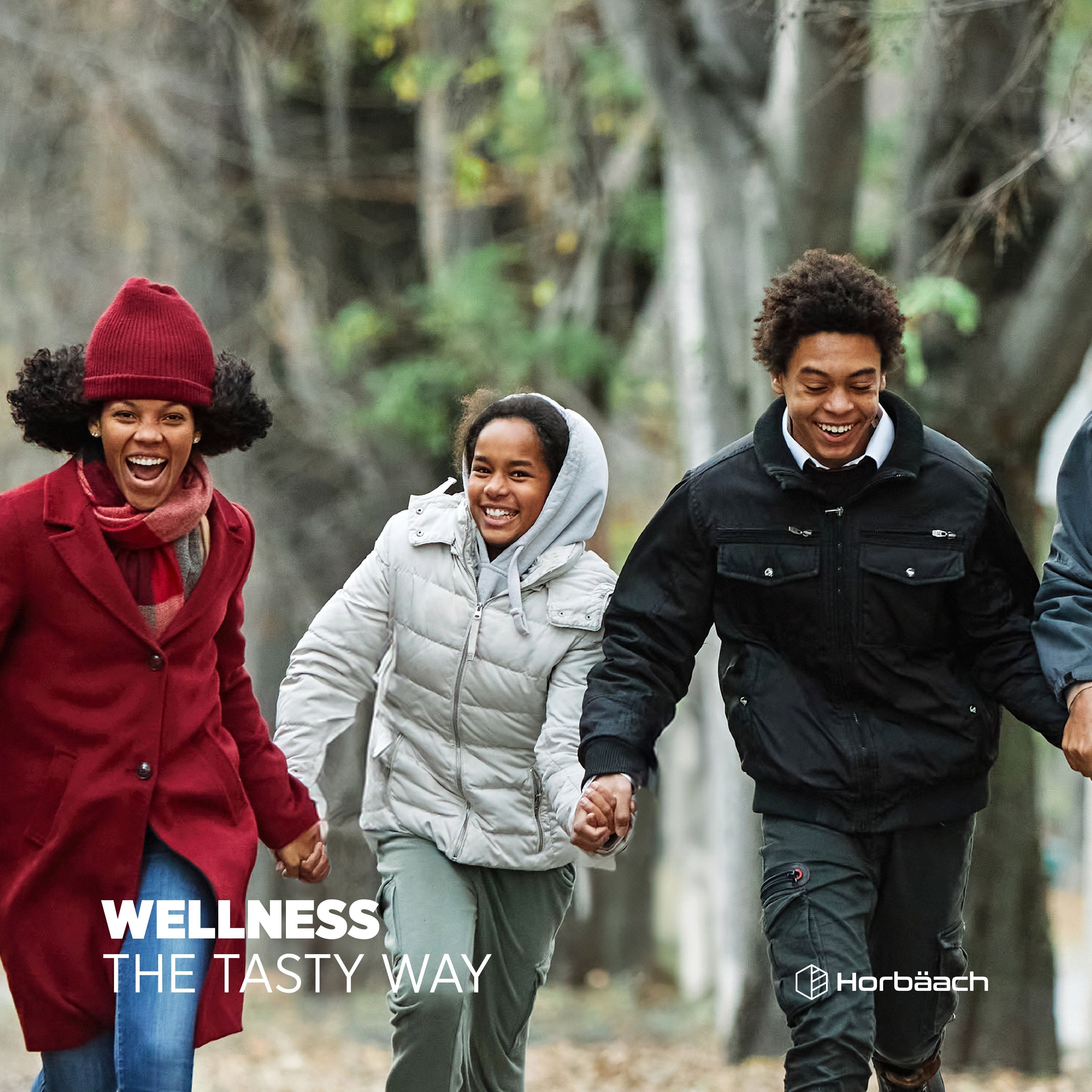 Three happy young people smiling and holding hands outdoors with text 'WELLNESS THE TASTY WAY'.